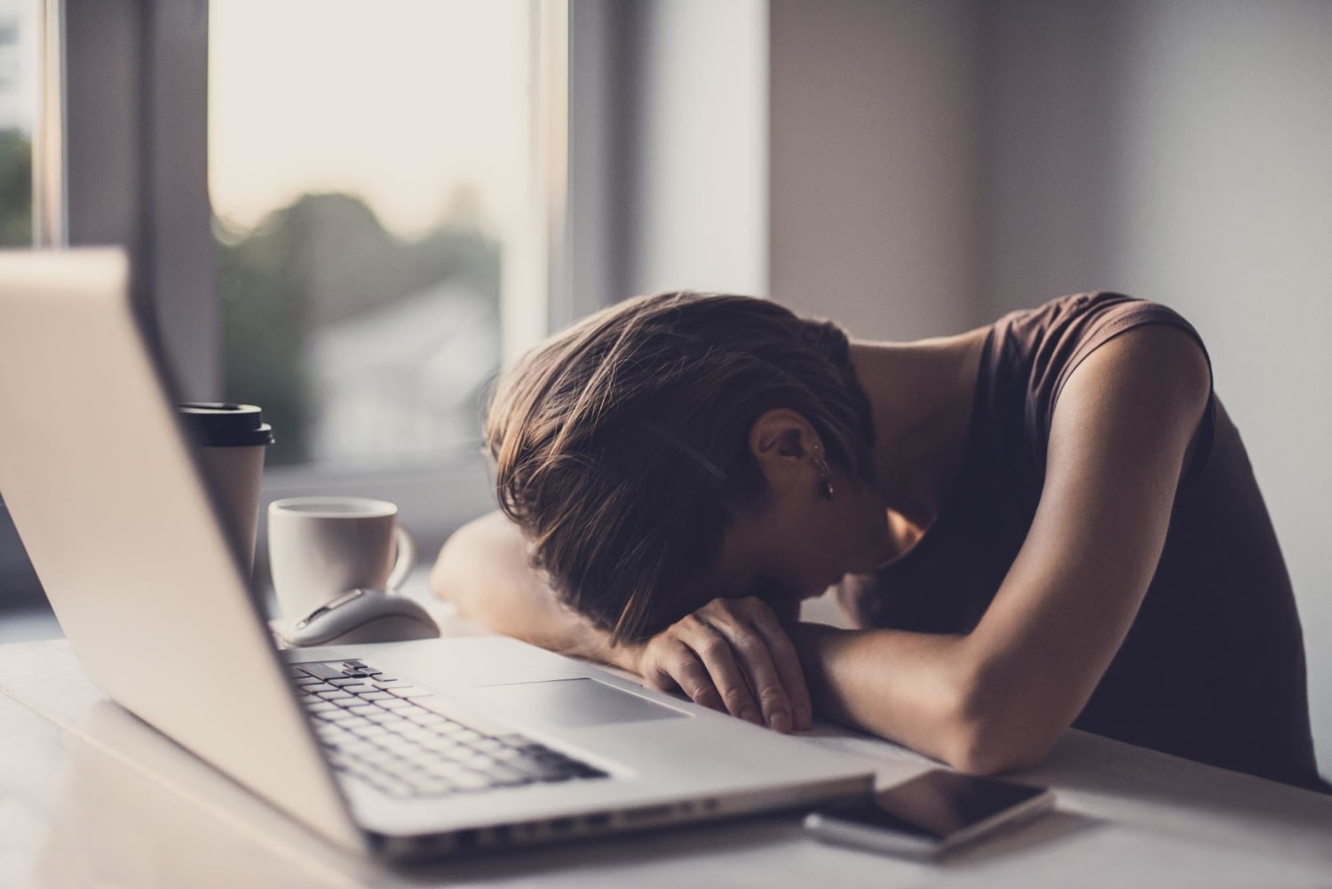 Junge Frau legt ihren Kopf erschöpft auf den vor ihr liegenden Laptop